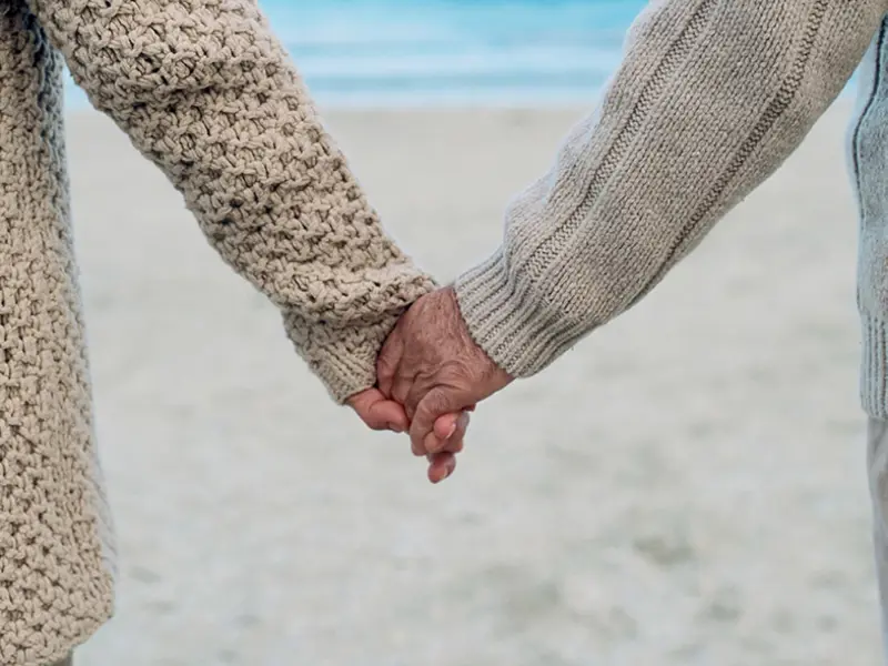 To personer holder hånd på en strand stående